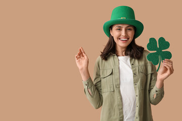 Beautiful young woman in leprechaun hat with clover on brown background. St. Patrick's Day...