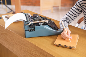 Female author with notebook and vintage typewriter at table in office, closeup