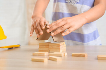 Little architect with building blocks at table in room, closeup