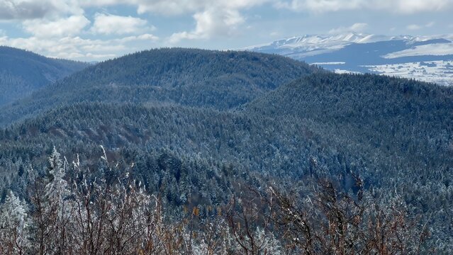Majestic Winter View from Puy de Dôme: Snow-Covered Mountains and Forests under a Cloudy Sky
