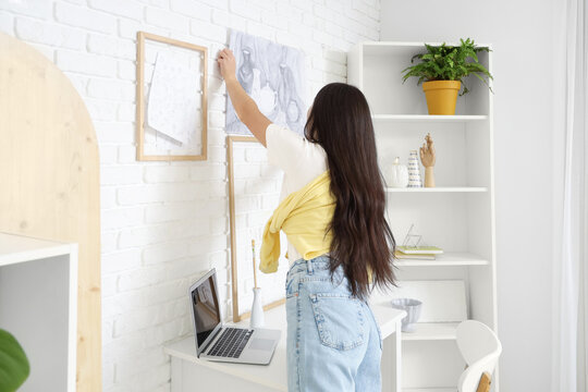 Female artist hanging her drawing on wall in workshop