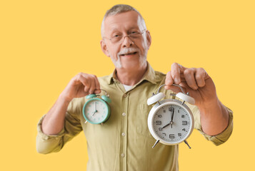 Mature man with alarm clocks on yellow background, closeup