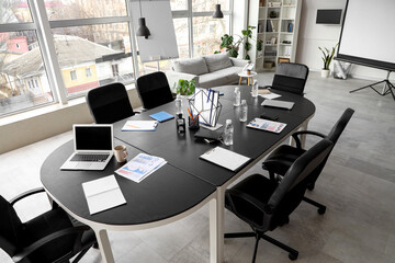 Table, armchairs, laptop and stationery prepared for business meeting in stylish conference hall