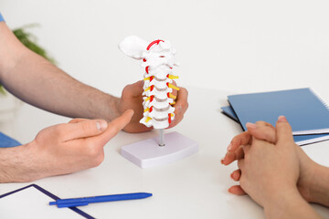 Male doctor explaining spinal anatomy with vertebral column model to patient in clinic, closeup