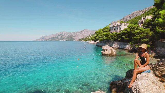 Woman on rocky beach with green pine trees and crystal clear sea waters. Contemplative girl enjoying nature landscape in Croatia.
