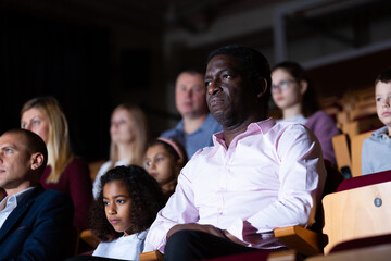 Portrait of interested african american theatergoer sitting in theater hall, watching theatrical...