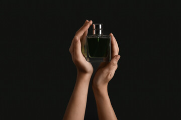 Female hands holding bottle of perfume on black background