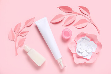 Bottles of cosmetic products, paper flowers and leaves on color background
