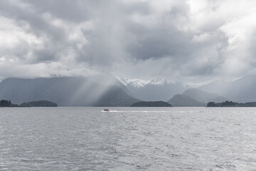 Naklejka premium Rod and line fishing Boat with God's rays and rain in the mountains behind, Sitka, Alaska, USA