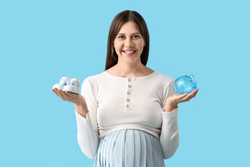 Young pregnant woman with piggy bank and baby booties on blue background. Maternal Benefit concept