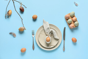 Beautiful table setting with Easter eggs and tree branch on blue background