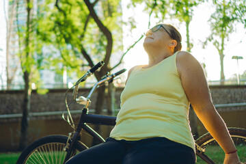 plus-size, middle-aged latin woman outside in a park breathing and sunbathing with her bicycle on her side