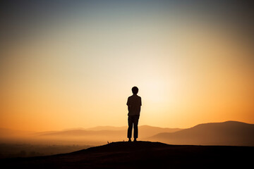 Fototapeta na wymiar Silhouette of a Lone Person Standing on a Cliff Overlooking a Sunset Sky. Contemplation and Adventure Concept