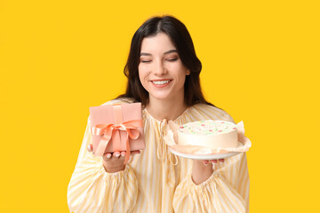 Happy young woman with sweet bento cake and gift box on yellow background. International Women's Day