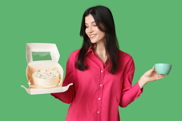 Beautiful young woman holding box with sweet bento cake and cup of coffee on green background....