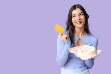 Beautiful young woman with sweet bento cake and credit card on lilac background. International...