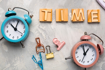 Text TIME with alarm clocks and paper clips on grey background. Time management concept. Closeup