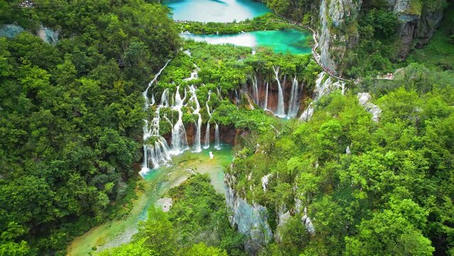 Mountain waterfall flows into a lake with many streams of water. People hiking on narrow path in Plitvice National Park Croatia.