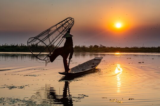 Fisherman at Inle Lake with traditional Intha conical net at sunset, fishing net, leg rowing style, Intha people, Inle lake, Shan state, Myanmar, Asia