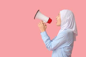 Young Asian Muslim woman shouting into megaphone on pink background. National Be Heard Day