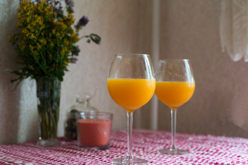 Two vine glasses of orange juise with candle and spring bouquet on the table. Cozy and easy lifestyle.