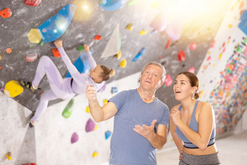 Young woman and adult man in sportswear posing on climbing wall