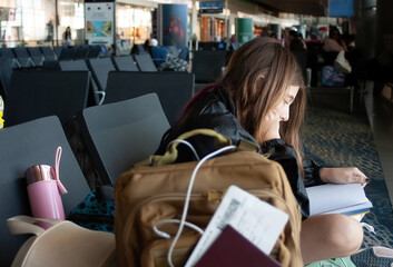 Young girl waits at the airport for the announcement of her plane departure reading a book.