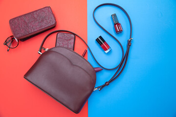 Woman's handbag in crimson color and accessories on red-blue background. Top view.