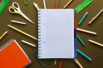 Open notebook with copy space for text on blurred dark background with variety of school supplies.