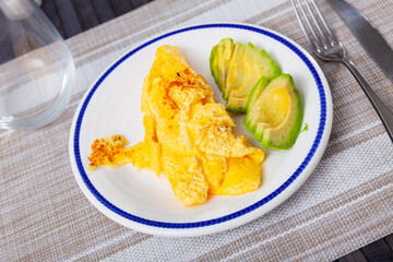 Idea for healthy and low-carb breakfast is omelette and half chopped avocado. Simple dish is served with appliances and aperitif glass.