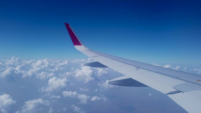 Jaipur, Rajasthan, India-October 25 2023; A Window view of an Aero plane wing gliding above the white clouds through the vibrant blue Sky in India.
