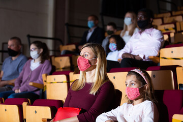 Young woman with preteen daughter wearing protective masks watching theatrical performance. Concept...