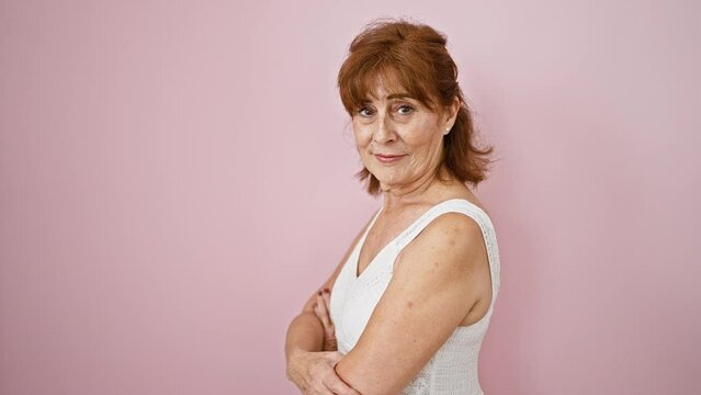 Confident middle-aged woman smirking in an elegant dress, standing offside with a natural, unforced smile. casually posed against an isolated popping pink wall.
