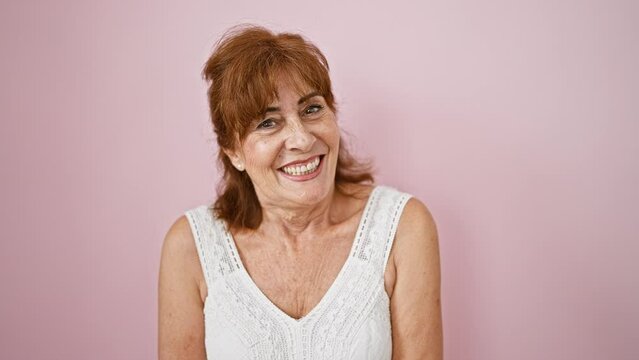 Cheerful and happy, middle age woman in a sexy expression caught winking at the camera! wearing a dress, standing isolated over a cute pink background.