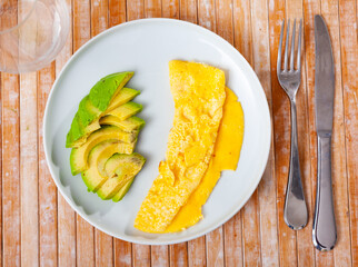 Idea for healthy and low-carb breakfast is omelette and half chopped avocado. Simple dish is served with appliances and aperitif glass.