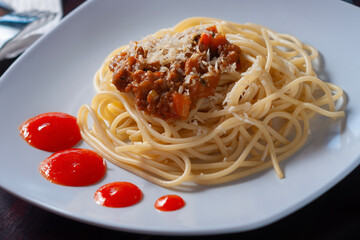 spaghetti bolognese with cheese sprinkled is placed on a white plate with a wooden background