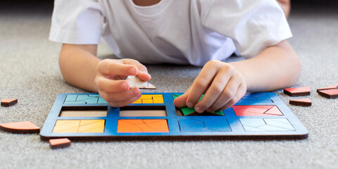 A boy is playing a logical wooden game on the carpet. Montessori educational toys, geometric puzzle