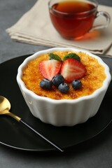 Delicious creme brulee with berries and mint in bowl on grey table, closeup
