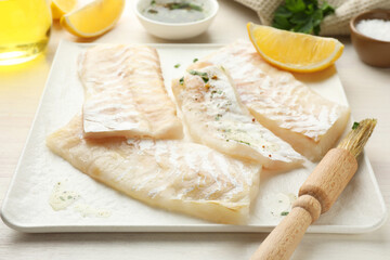Fresh raw cod fillets with spices, lemon and brush on white table, closeup
