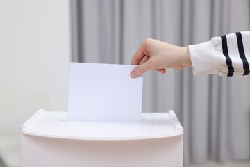 Woman putting her vote into ballot box on blurred background, closeup