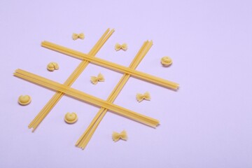 Tic tac toe game made with different types of pasta on lilac background