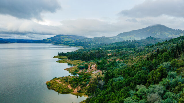 Aerial view of serene Embalse de Tomin&eacute;, Guatavita, Cundinamarca, surrounded by lush greenery and mountains under a cloudy sky