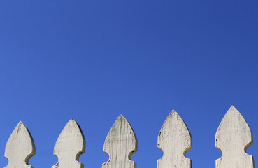 Top of a weathered white fence against a clear blue sky background