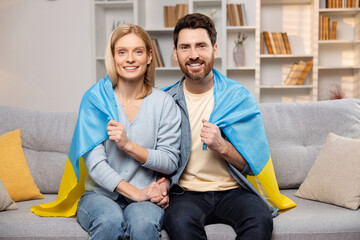 Happy Ukrainian family in their home, proudly displaying the Ukrainian flag, hands intertwined