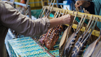 Poyrait buyer's hand choosing smoked fish at the market. Smoked fish clamped with bamboo which is...