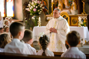 Priest giving mass to a group of children on communion day in a Christian church - obrazy, fototapety, plakaty