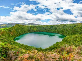 Breathtaking view of serene Laguna de Guatavita, lush greenery under vibrant sky in Guatavita,...