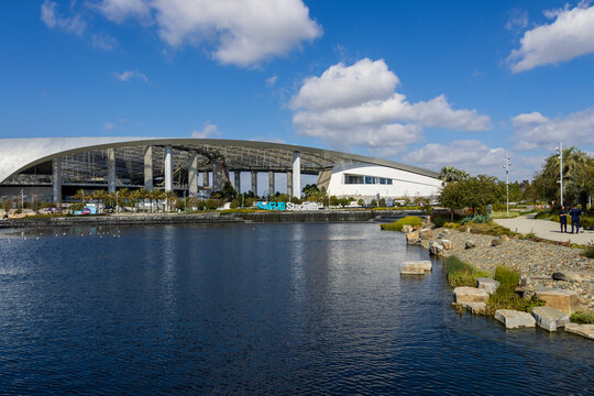 A beautiful spring landscape at SoFi Stadium with lush green palm trees and plants, a lake with birds swimming, blue sky and clouds in Inglewood California USA