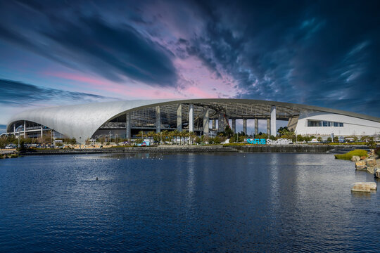 A beautiful spring landscape at SoFi Stadium with lush green palm trees and plants, a lake with birds swimming and powerful clouds at sunset in Inglewood California USA