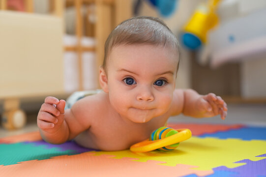 Adorable smiling cute funny happy infant baby in diaper crawling and playing on the floor on a developing foam puzzle play mat with toys in nursery room. Healthy child concept. Baby goods packaging
